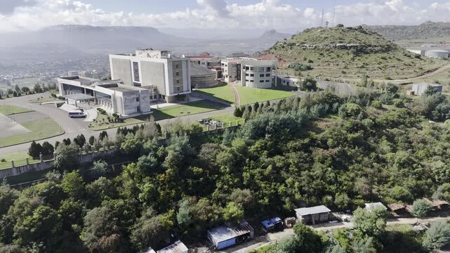 Drone orbits to the right in wide shot of west side of parliament building atop a hill on a sunny morning in Maseru, Lesotho