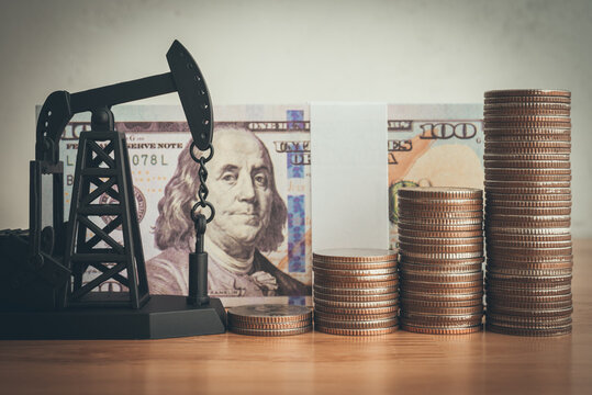 Rising up stack coins and oil pumpjack with US banknote background. World petroleum and energy industry or trading commodity investment, crude oil and gas price increase from war effect concept.