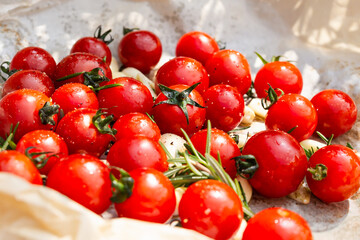 Fresh red cherry tomatoes with rosemary sprigs and garlic cloves on baking paper. © bignai