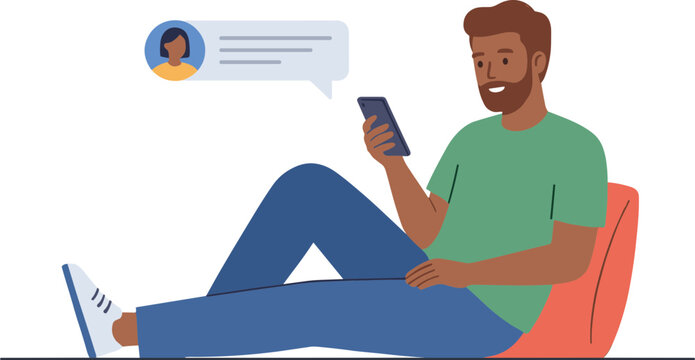 A man sits on a chair laughing while texting on his phone.