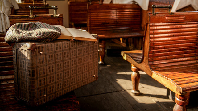 Vintage suitcase with flat cap and open book on wooden train seats