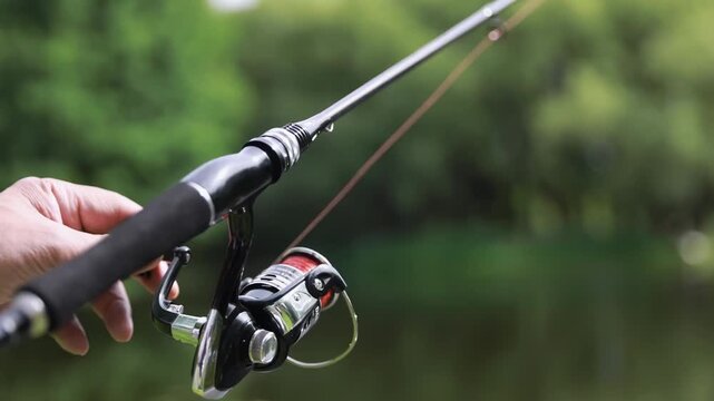 Fisherman hold fishing rod with spinning reel attached, trying to do perfect cast, throwing lure, excitement angling on shore of lake with green shores on summer vacation, hobby catching fish outdoors
