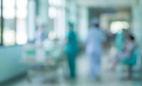 A blurred view of a hospital corridor showing healthcare professionals and patients in a busy medical environment, conveying a sense of urgency and care.