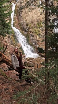 A woman against the backdrop of a mountain waterfall.