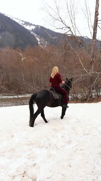A woman on a horse in the snowy mountains with a mountain river in the background. Excursion, mountain trip.