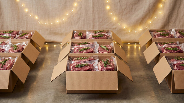 Cardboard boxes with vacuum‑sealed meat and herbs symbolizing premium charity food packaging, artisanal delivery, and festive culinary traditions