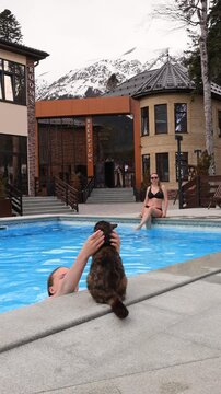 Traveling with a pet. A happy mother and daughter swim in a thermal hot pool against the backdrop of snow-capped mountains.