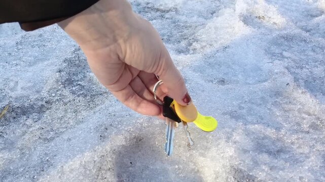 A hand picks up the lost keys to the apartment from the snow in winter. A woman found the keys on the road
