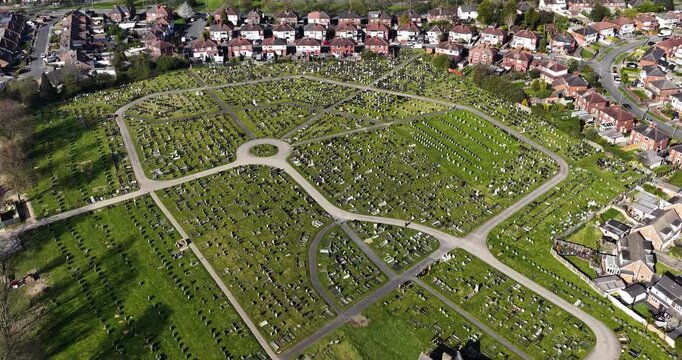 Aerial view of a cemetery in the town of Seacroft Leeds West Yorkshire with rows of gravestones curved paths church building and surrounding housing estates captured from above in the spring time