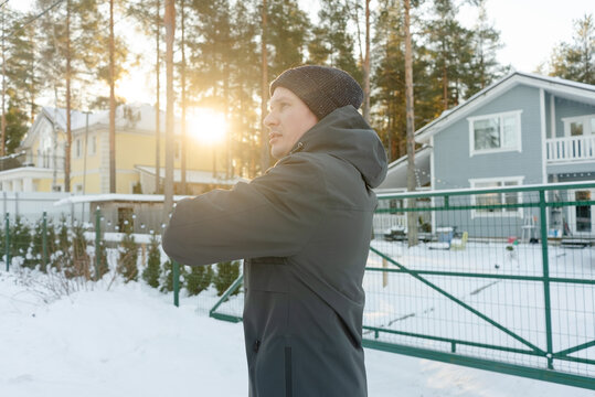 A guy in his forties does upper body twists outdoors. He prepares for a run in cold weather, caring for his spine and core muscles.