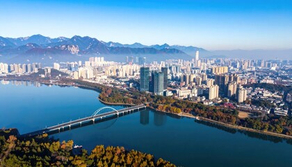 Obraz premium An aerial view showcases a sprawling cityscape nestled beside a serene lake, framed by majestic mountains under a clear blue sky.