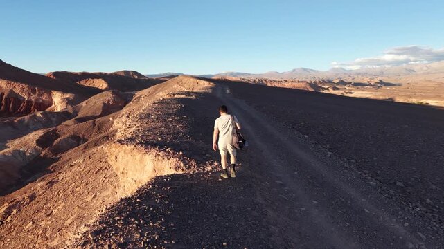 Cinematic drone shot follows TV Host of DIY Destinations Charles Huang as he walks along a narrow desert ridge in the Mars Valley (Valle de Marte) near San Pedro de Atacama, Chile, during golden hour