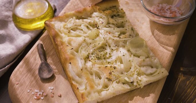 Traditional Italian onion focaccia on wooden board with olive oil and pink salt. High-angle video captures authentic Mediterranean bakery texture and rustic homemade aesthetic under warm natural