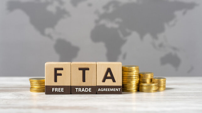 A wooden block arrangement spelling FTA, surrounded by gold coins on a white surface with a gray world map in the background.