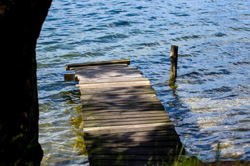 Drewniany stary pomost molo na pofalowanej wodzie przy brzegu jeziora. © Monika