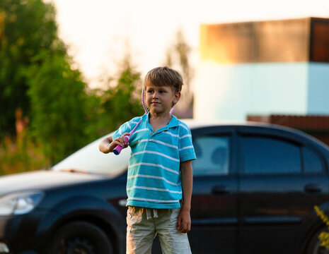A young boy stands waiting for the start of a badminton game outdoors on a sunny summer day. Active play, coordination, and fun vacation time in nature with green grass.