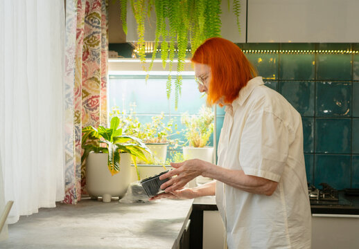 A woman in her seventies with red hair is absorbed in her hobby of planting new seeds. The image shows her focus and enjoyment in gardening. Grandma starting new growth.