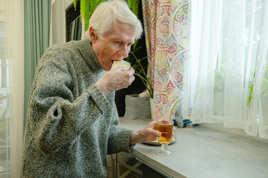 An older adult savors his breakfast of tea and butter sandwich at kitchen counter. The image emphasizes enjoyment and comfort of morning meal. Grandpa content and relaxed.