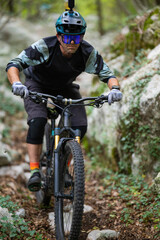 Fototapeta premium Focused mountain biker riding a full-suspension bike on a rocky forest trail wearing helmet and goggles