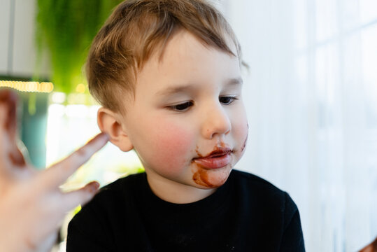 Extreme close up of a three year old child with face covered in melted chocolate. Messy cheeks and mouth after eating forbidden sweets. Concept of unhealthy diet, allergies, diabetes