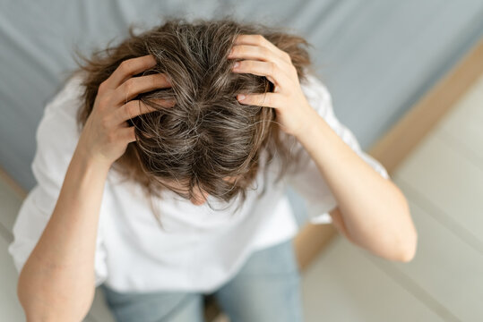 A woman reacts with surprise to suddenly discovering new gray hairs on her head. The mature adult was not expecting silver strands to appear so quickly. Mother faces unexpected sign of aging.
