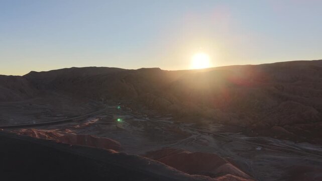 Cinematic flying toward the setting sun over the jagged peaks of Mars Valley (Valle de Marte) and tilting down to reveal the otherworldly red terrain near San Pedro de Atacama