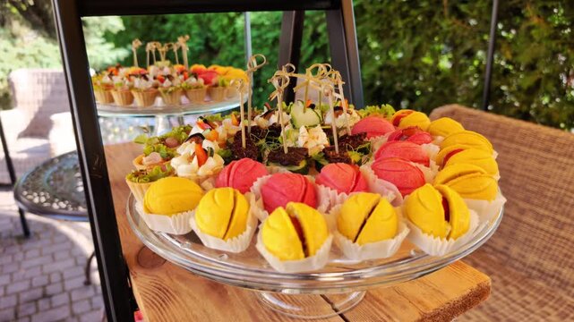 Elegant arrangement of yellow and pink meringue cookies, alongside assorted savory canapes and mini quiches, presented on glass platters for reception or party
