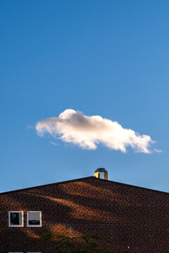 Brick rooftop architecture on a building with minimal pattern and rich texture lit by sunlight as a single cloud drifts in blue sky
