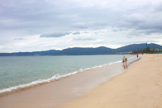 Chinese couple walks along sandy shoreline at Yalong Bay, Hainan Island. Travel to China, Chinese Hawaii, tropical bay, resort landscape.