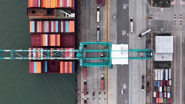 Top-down drone view of colorful shipping containers and cranes at busy port terminal.
