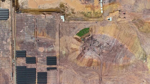 High-angle drone shot of large solar farm construction with panels, earthworks, and heavy machinery.