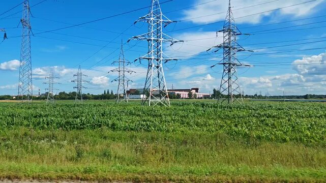 Side view of power lines in the countryside from a car window. Moving view from train shows parallel road and rural landscape. Power lines and window reflections visible during fast transit.