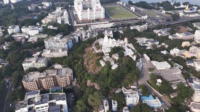 Aerial footage of the Birla Mandir perched on a hill in the centre of Hyderabad, Hussain Sagar Lake surrounded by dense greenery and winding access roads, with the grand Telangana State Secretariat