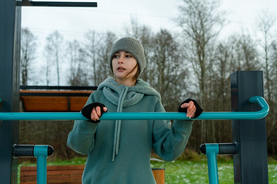 Close-up shot of a sporty womans face and hands as she tightly grips the handlebar of an outdoor leg trainer. moment of maximum effort, showcasing dedication to winter fitness and strength.