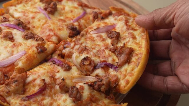 Thin crust pizza topped with chicken, cheese, and chives on a wooden plate, getting picked from table.