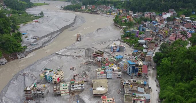 Drone shot of houses buried in silt near the Melamchi River after flooding, surrounded by forest and damaged landscape in Sindhupalchowk Nepal.