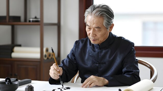 38. A 45-year-old Chinese calligraphy master with calm focused features and silver-streaked hair sitting at a traditional wooden desk, natural diffused window light illuminating the scene, wearing a s