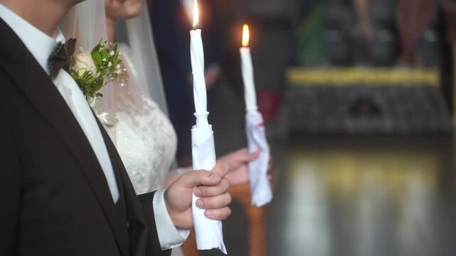 Lit candles in hands of spouses at Wedding Sacrament in Orthodox Church