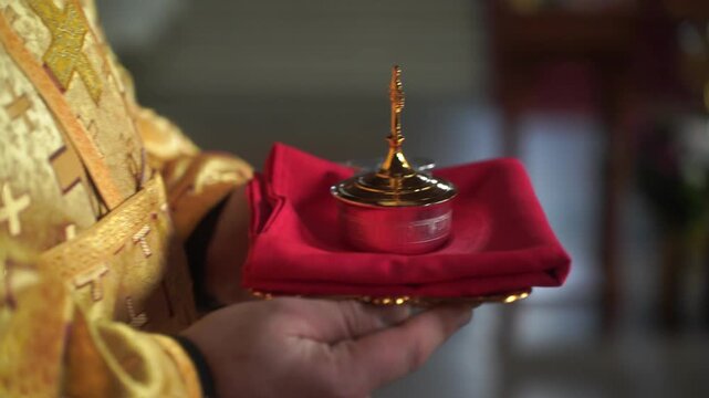 Intimate shot of an Orthodox Christian wedding ritual showing a golden chalice filled with water, wedding rings, delicate white roses, and ornate lace, symbolizing faith