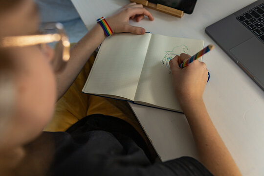 Creative teenager drawing in notebook at home in cozy bedroom