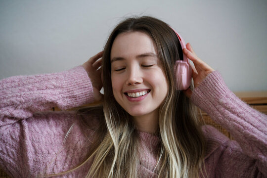 Smiling young womarelaxing at home listening to music on headphones