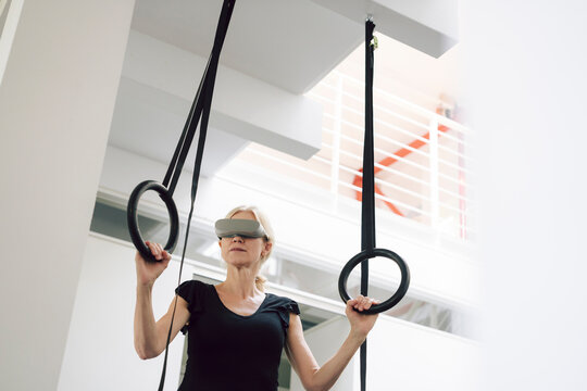 Woman using VR headset while training with gymnastics rings indoors