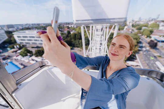 Smiling woman taking selfie on Ferris wheel at summer fair