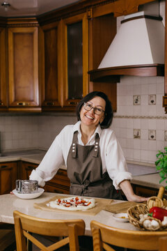 Smiling woman in apron baking homemade pizza in a cozy kitchen