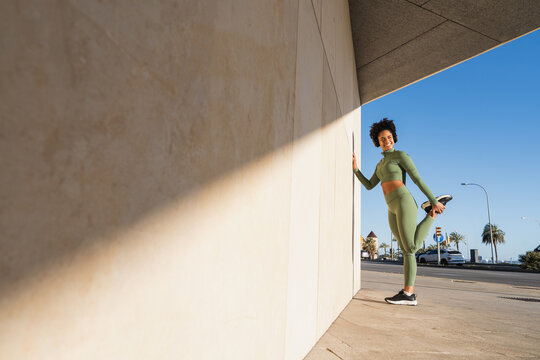 Athlete in green sportswear stretching outdoors against modern wall