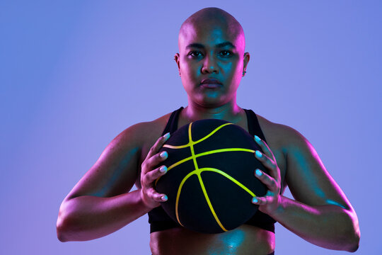 Bald athlete holding a basketball in a studio setting with purple lighting