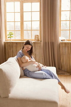 Mother breastfeeding baby on sofa in cozy Scandinavian living room