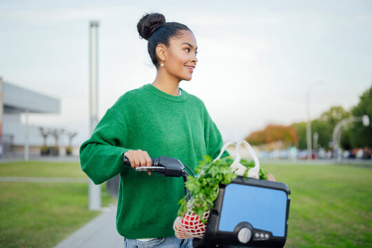 Woman riding electric bike with groceries in urban setting outdoors