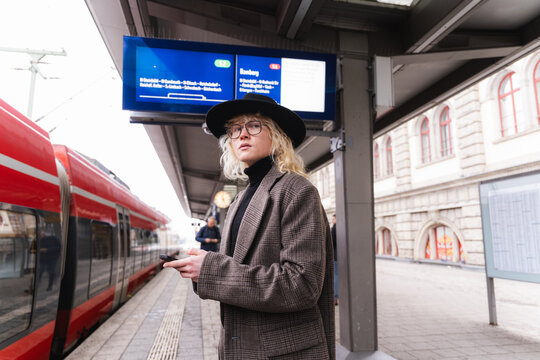 Young man waiting with smartphone at urban train station platform