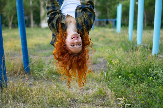 Woman with red curly hair smiling upside down at old outdoor playground
